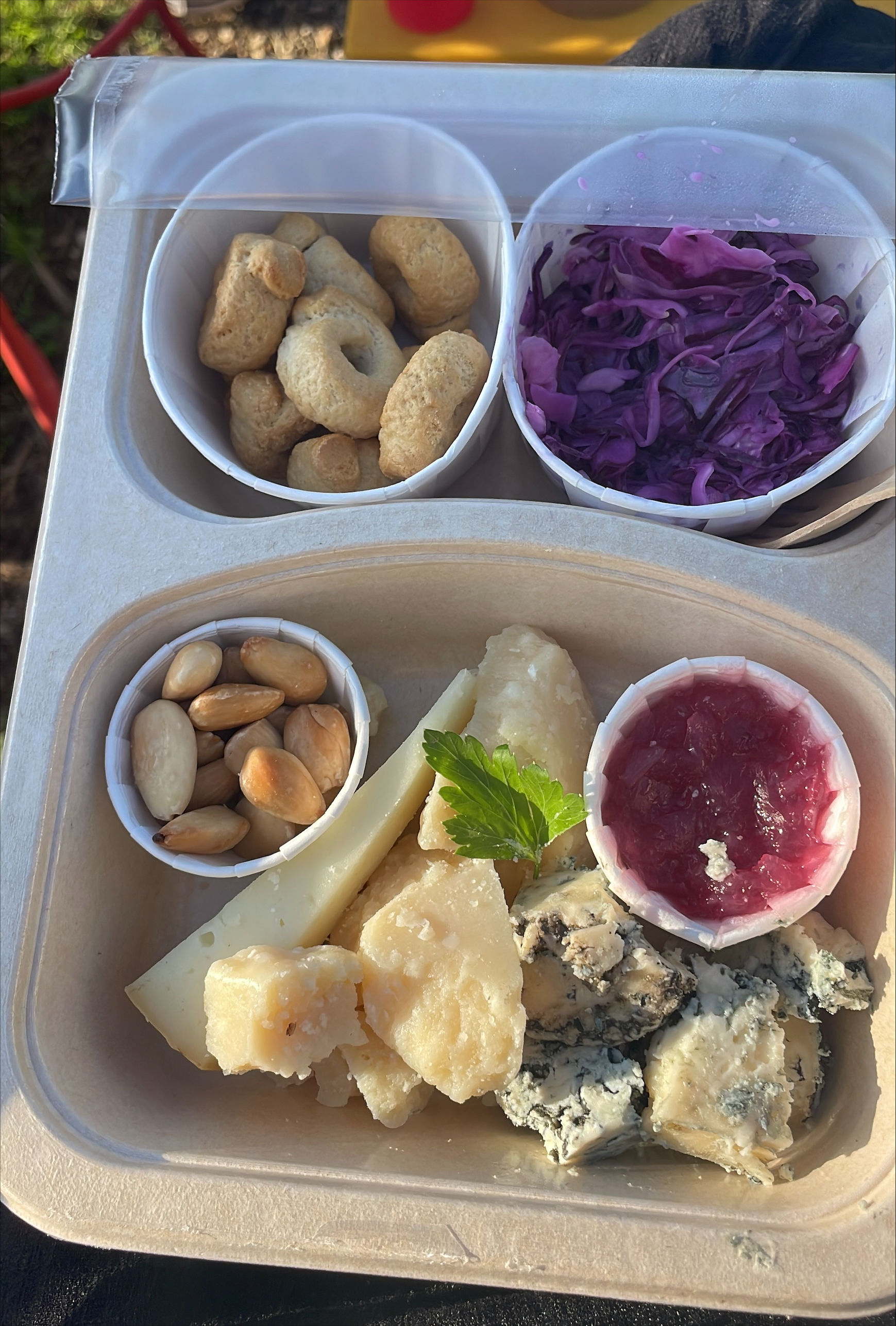 A box of food with bread, cheeses, jam, cabbage, and nuts.
