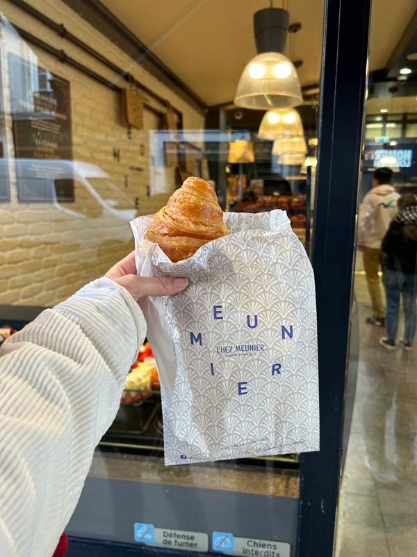 CEA CAPA student holding fresh croissant in front of cafe window