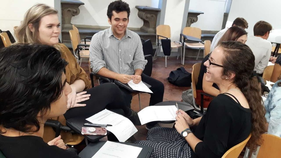 Group of students sitting in classroom desks talking and smiling