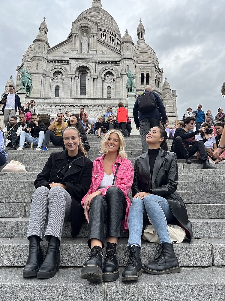 Three students sitting on stairs of Sacre Coeur in Paris on a gloomy, cloudy day.