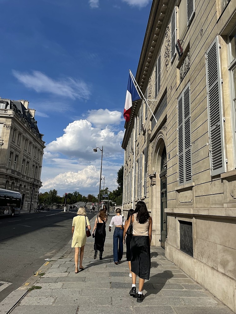 Group of 4 student friends walking down Parisian streets next to beige building
