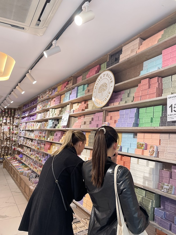 2 student friends shopping & looking at blue, orange, green, pink, purple soaps in Paris