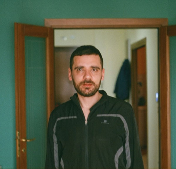 Italian man poses in front of door frame and green wall
