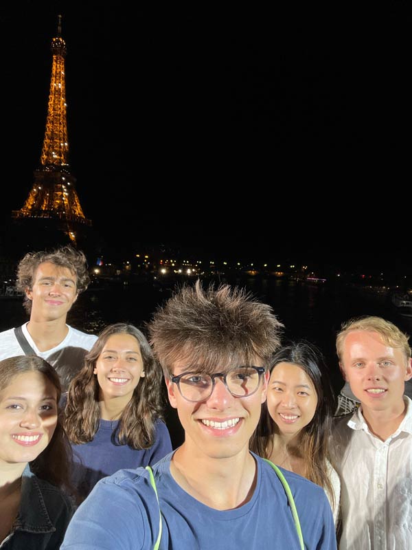 group of 6 students in front of twinkling lights at Eiffel Tower at night